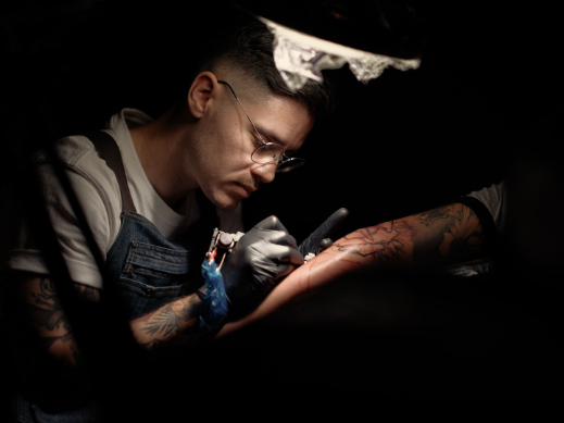 Artist tattooing under a lamp, gloved and focused